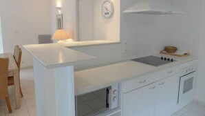 Et moderne køkken med en central ø, hvide skabe, en indbygget ovn og et ur på væggen.