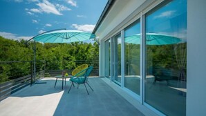 En moderne balkon med glasdøre, et bord, to stole og en blå parasol.