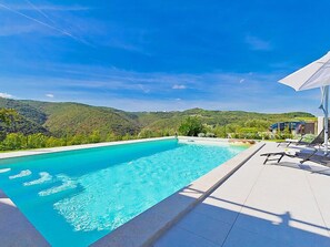 Ein Schwimmbecken mit klarem, blauem Wasser, umgeben von einer gefliesten Liegefläche und Liegestühlen.