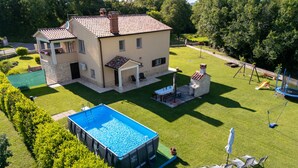Una casa de dos pisos con piscina, zona de barbacoa y juegos infantiles.