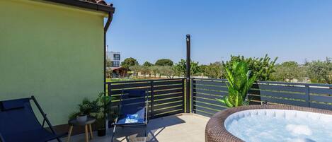 A rooftop terrace with a hot tub, a chair, and a small table with a plant.