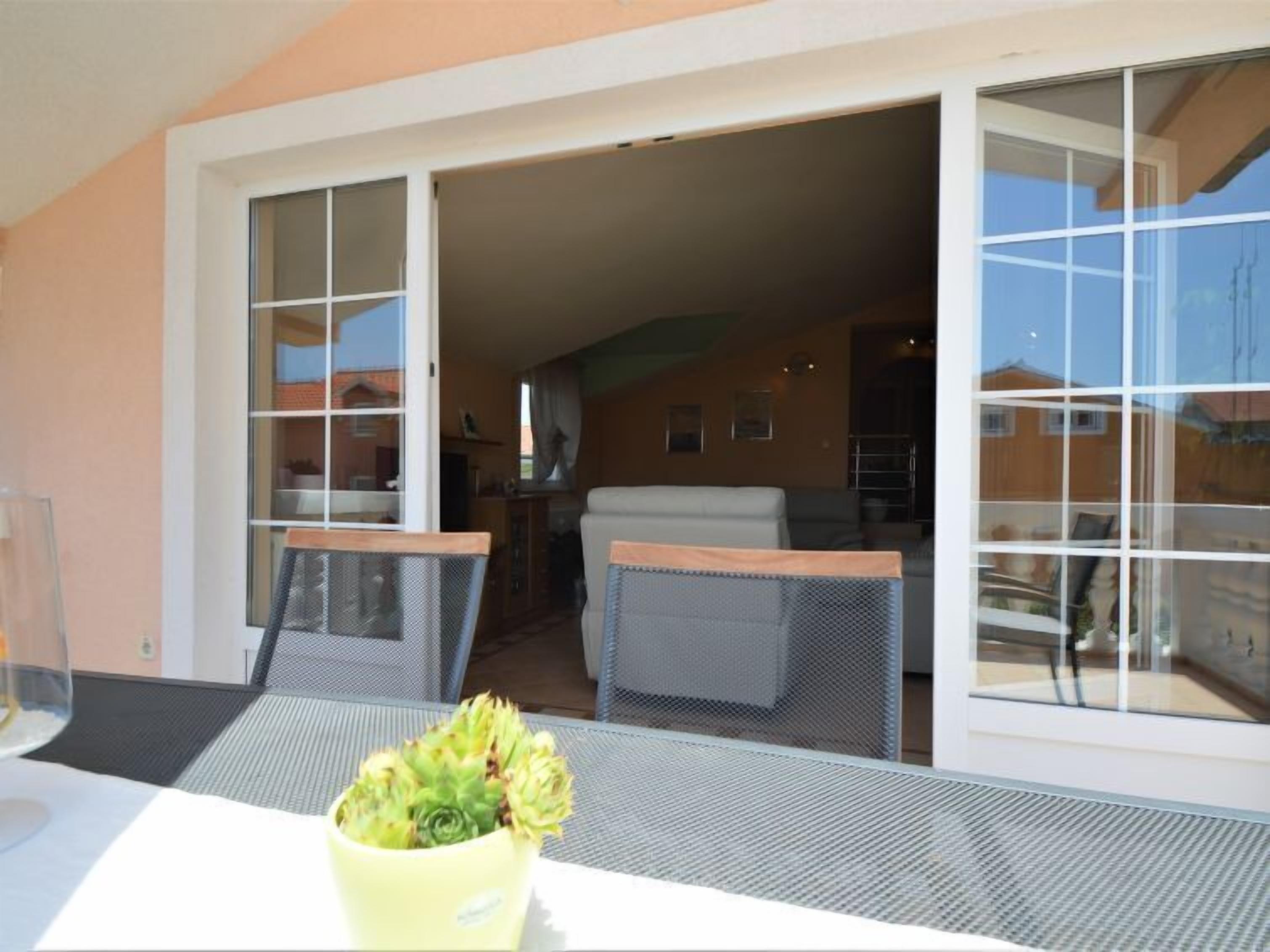 A patio area with a table and chairs, a yellow pot with a plant, and a sliding glass door leading to an indoor living space.