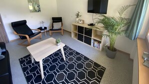 A living room with a black and white patterned rug, two black leather chairs, a wooden coffee table, a bookshelf, a TV, and a potted plant. - Apartments Carmena by Interhome (Saas-Grund)