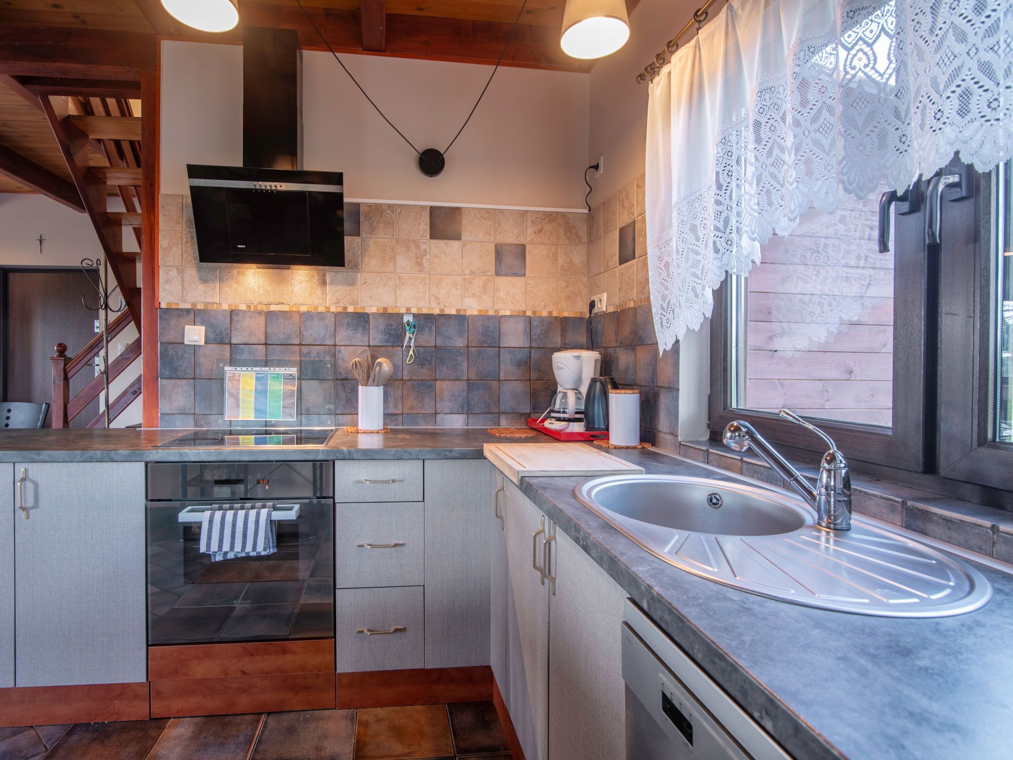 Een moderne keuken met een inbouwvaatwasser, een RVS spoelbak en een flatscreen televisie boven het fornuis.