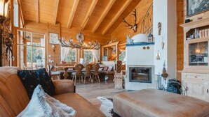 Ein gemütliches Blockhaus-Interieur mit Holzbalkendecke, Kamin, Essbereich und Geweih-Dekorationen.