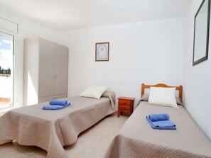Une chambre avec deux lits simples, une armoire, une petite table de chevet et un tableau encadré au mur.