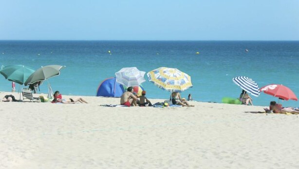 Une plage où des gens se détendent sous des parasols colorés, avec un ciel dégagé et une mer calme.