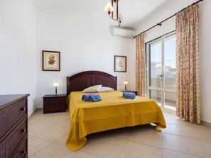 Une chambre d’hôtel comprenant un lit, deux tables de chevet, une commode, une fenêtre avec des rideaux et un luminaire au plafond.