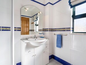 Une salle de bain avec des carreaux blancs, un lavabo, un miroir et un porte-serviettes.