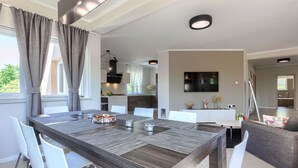 Un espace repas moderne avec une table en bois, des chaises blanches et une cuisine en arrière-plan.