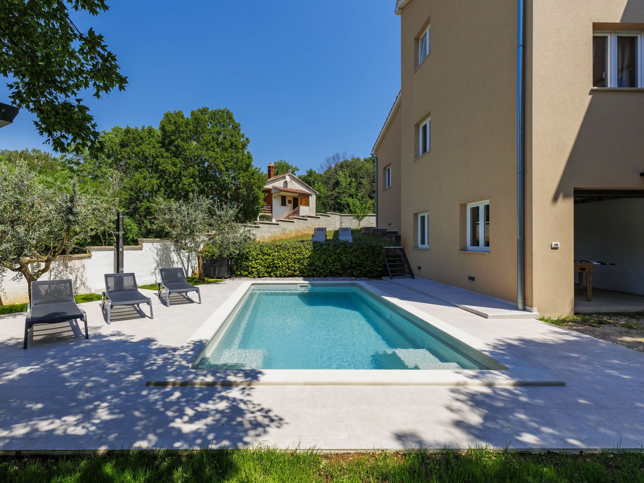 Ein rechteckiger Pool mit Liegestühlen, ein kleines Haus im Hintergrund und ein Gebäude mit Garage.