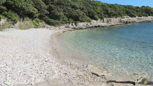 Una playa de guijarros con agua cristalina y afloramientos rocosos.