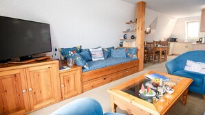 Una sala de estar acogedora con un televisor de pantalla plana grande, un sofá azul con cojines estampados, muebles de madera y una mesa de centro de vidrio.