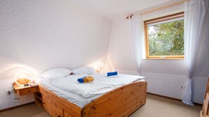 Una cama de madera con ropa de cama blanca, una mesita de noche con una lámpara y una ventana con cortinas.