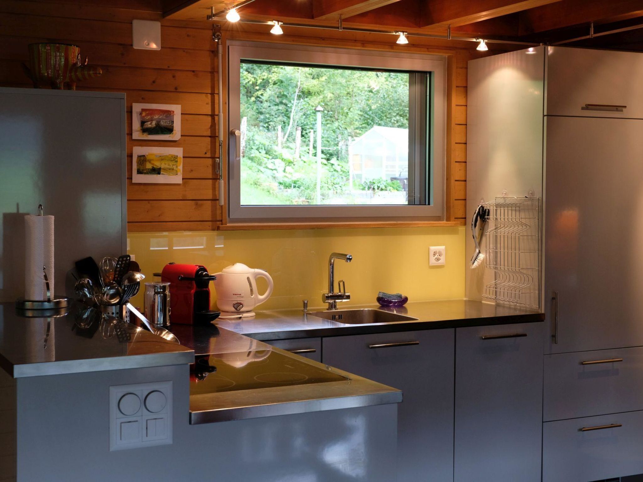 Una cocina compacta con ventana, paredes de madera, un refrigerador de acero inoxidable y un lavamanos.