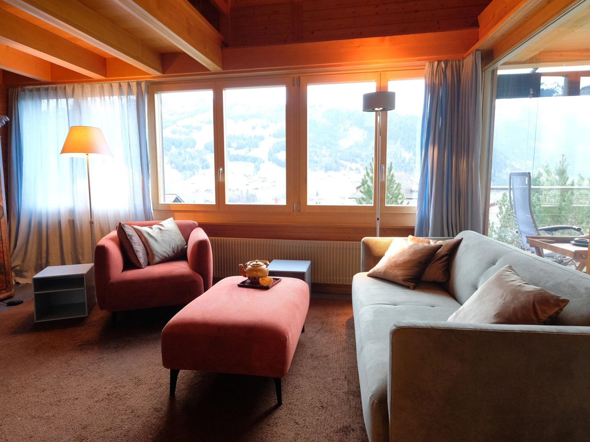 A cozy room with two sofas, a table, and a lamp. Large windows offer a view of the outdoors.