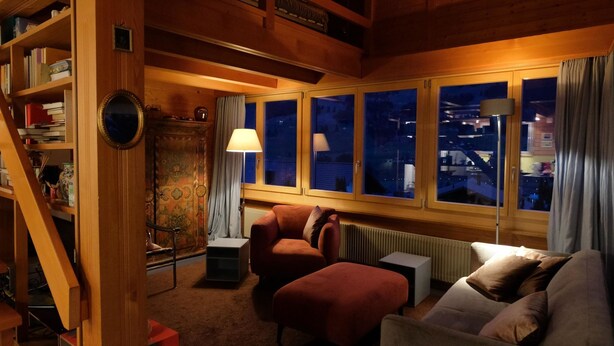 Una habitación acogedora con una escalera de madera, un sofá, una silla y una ventana con vistas a la ciudad de noche.