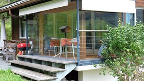 Una casa moderna con fachada de vidrio, terraza de madera y comedero para pájaros.
