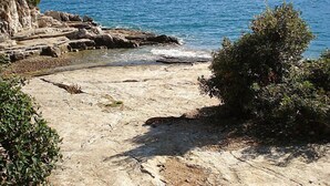 Costa rochosa com águas azul-claras e uma montanha ao longe.