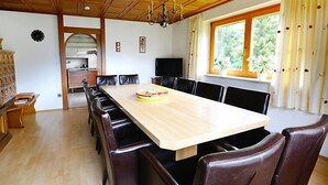 En matplats med ett träbord och stolar, en kristallkrona, en klocka och ett fönster med gardiner.