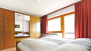 Ett hotellrum med två sängar, en garderob i trä, ett stort fönster med röda gardiner och ett vitt tak.
