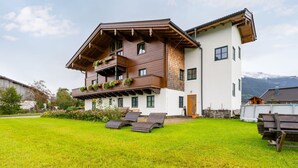 Een chalet met twee verdiepingen, een houten balkon, een verzorgd gazon en een berg op de achtergrond.
