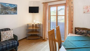 Een knus interieur met een houten tafel, een bank, een aan de muur bevestigde televisie en een raam met gordijnen.