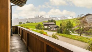 Een houten balkon met uitzicht op een landelijk landschap, inclusief een huis en bergen op de achtergrond.