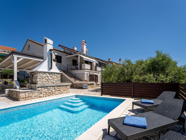 A swimming pool with lounge chairs, a stone wall, and a building with a balcony. - Albaneze by Interhome (Krk/Njivice)