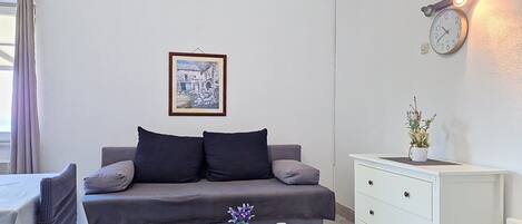 A modern living room with a grey sofa, a white coffee table with a vase, a white dresser, and a wall-mounted clock.