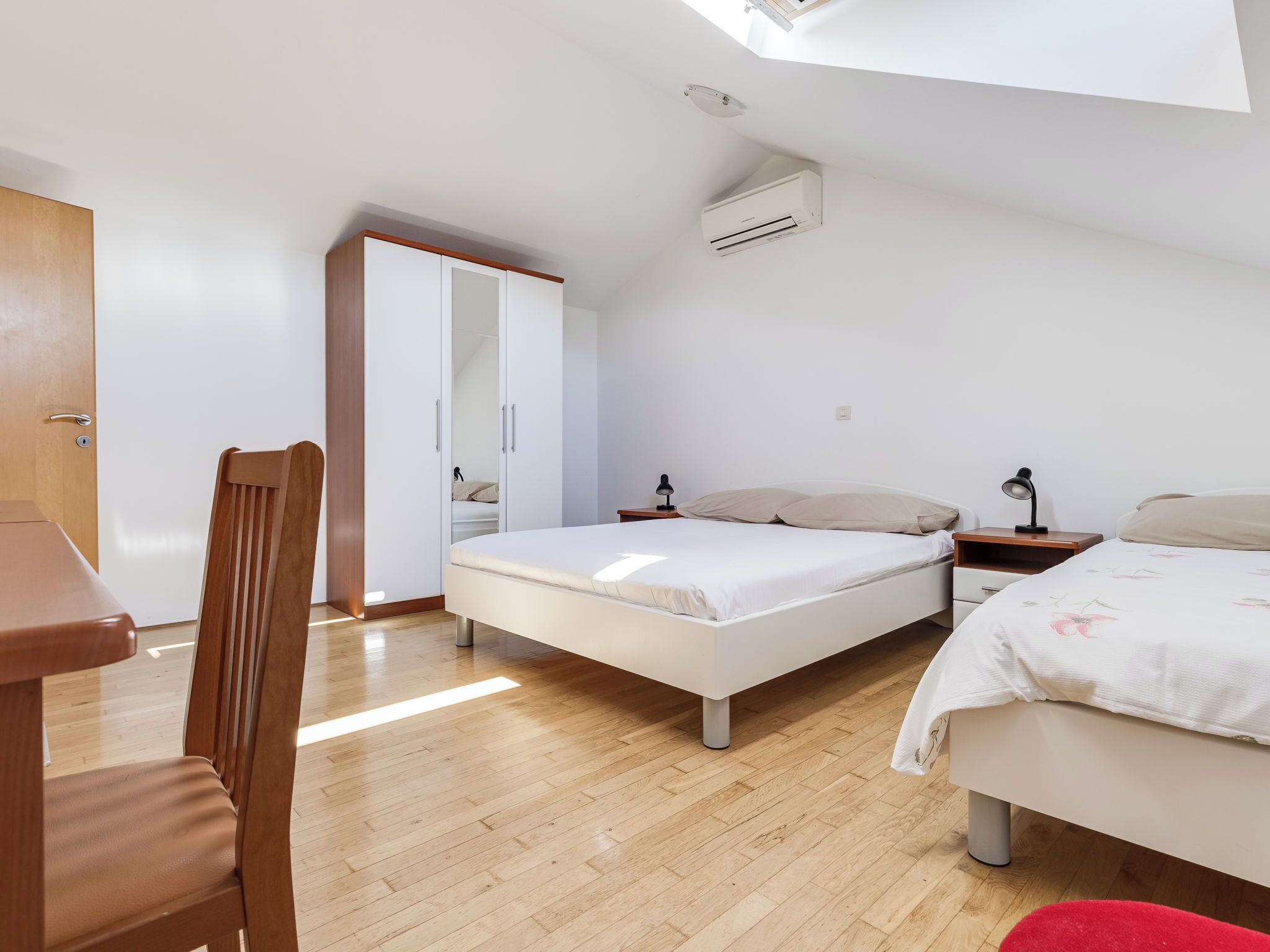 A bedroom with two beds, a wooden chair, a desk, and a wardrobe.