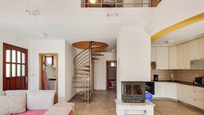 Um interior moderno com uma escada em espiral, uma cozinha com armários brancos e um sofá com um cobertor rosa.