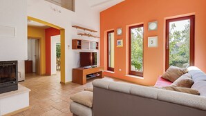 Sala de estar com lareira, televisão e sofá. Janelas com vista para o verde.