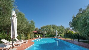 Piscina retangular com água azul cristalina, rodeada por um deck de madeira e cadeiras de lounge brancas.