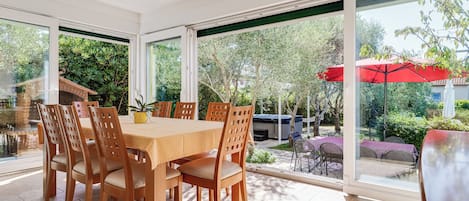A spacious patio with a wooden table and chairs, large windows, and a red umbrella.