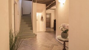 Un corridoio con una scala, un vaso di fiori su un tavolino rotondo e un lampadario a parete.