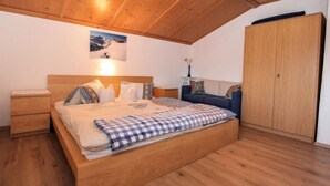 Un dormitorio con techo de madera, una cama con ropa de cuadros, una mesita de noche, un aparador y un armario grande.