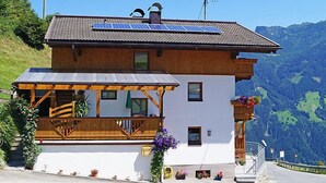 Una cabaña de dos plantas con techo inclinado, paneles solares y un balcón con barandilla de madera.