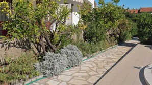 A white building with a balcony, surrounded by various plants and a stone pathway. - Apartment Vesela by Interhome (Vir)