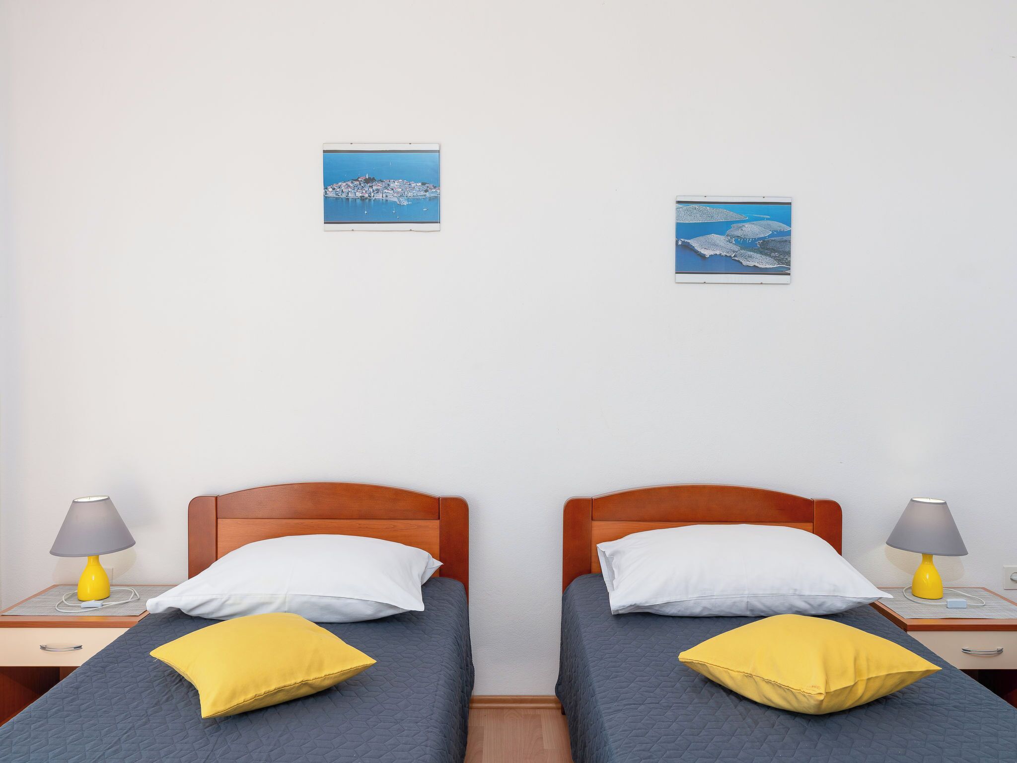 Hotellihuoneessa on kaksi sänkyä, joissa on molemmissa puinen pääty. Sängyissä on valkoisia ja keltaisia tyynyjä sekä sininen, kuviollinen peitto. Huoneessa on kaksi yöpöytää, joissa on lamput, ja seinällä on kaksi kehystettyä kuvaa.