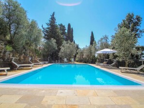 A rectangular swimming pool with clear blue water, surrounded by stone tiles.