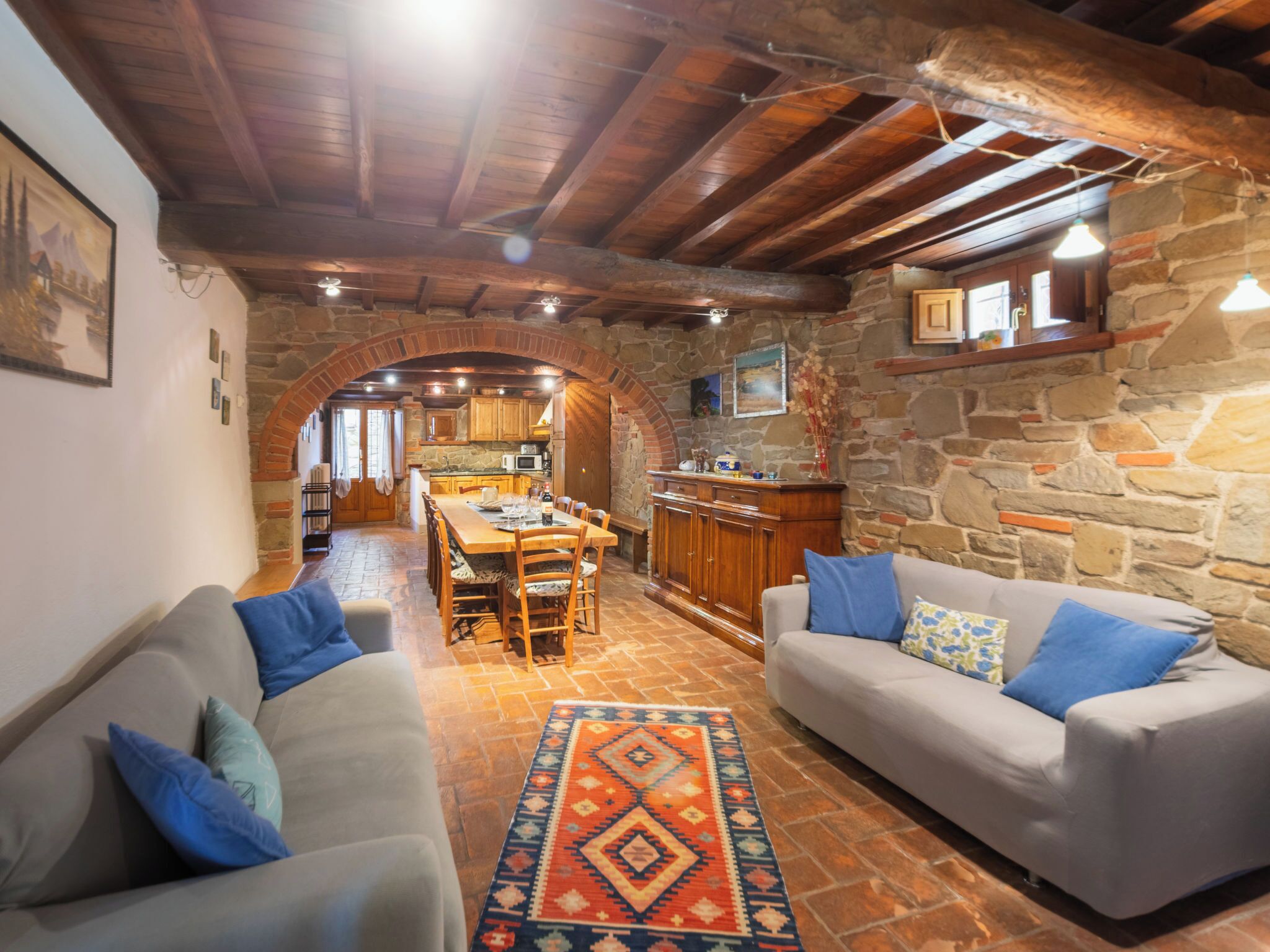 A cozy living area with a stone fireplace, wooden ceiling beams, and a dining table set for four.