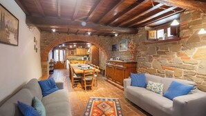 A cozy living area with a stone fireplace, wooden ceiling beams, and a dining table set for four.