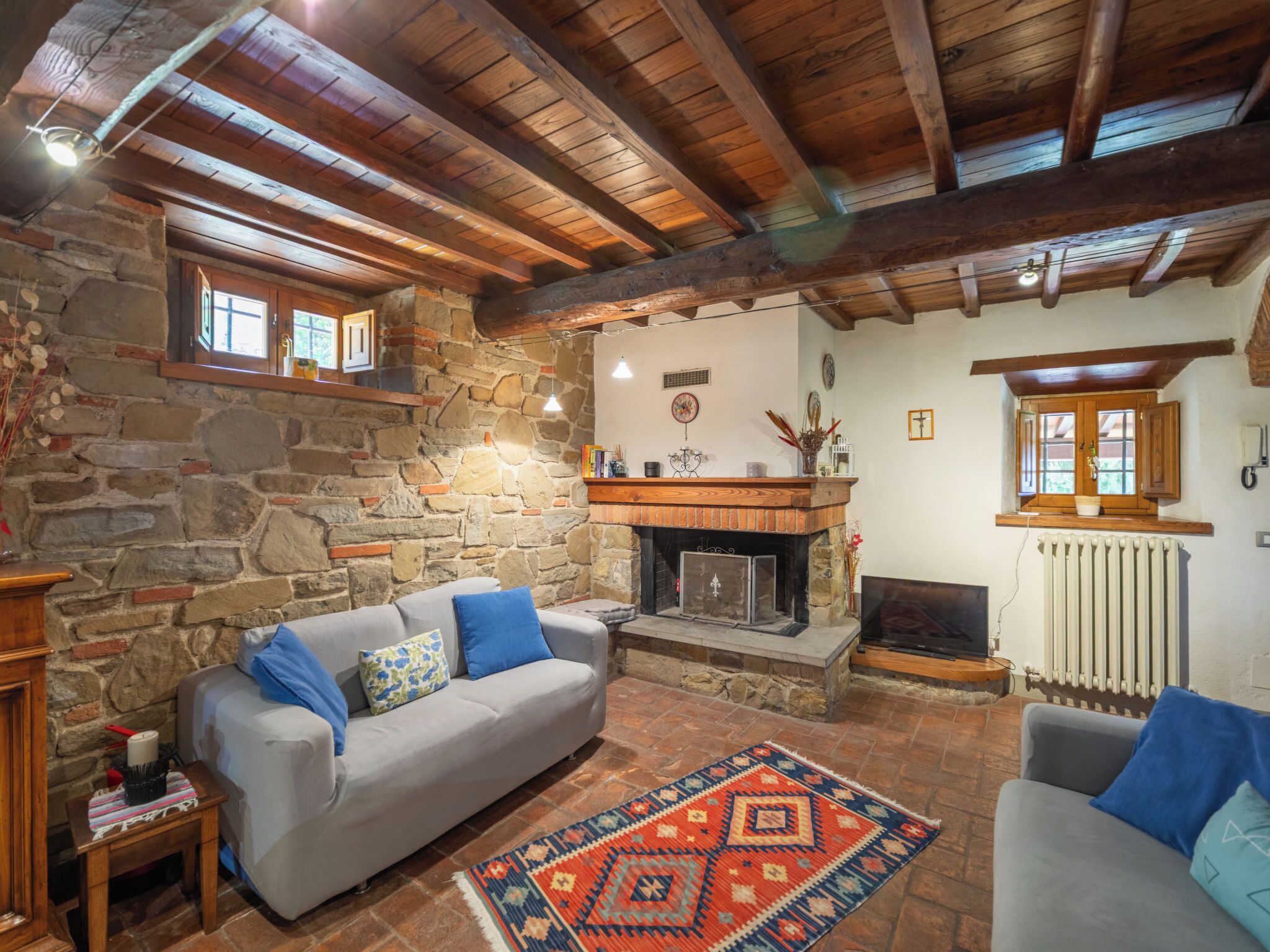 Una sala acogedora con pared de piedra, chimenea, sofá y alfombra estampada.