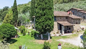 A stone house with a tiled roof, surrounded by a well-maintained garden with various plants and a large tree.