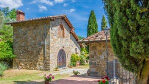 A stone building with a tiled roof, a small garden with potted plants, and a clear sky.