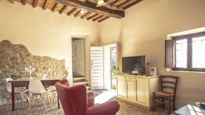 A cozy room with a stone wall, a red armchair, a television on a wooden cabinet, and a window with a view.