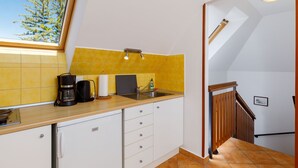 Een keuken met een raam, gele tegels, een koffiezetapparaat en een spoelbak.