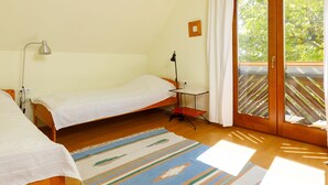Slaapkamer met twee eenpersoonsbedden, een bureau, een stoel, een lamp en een schuifdeur naar een balkon.