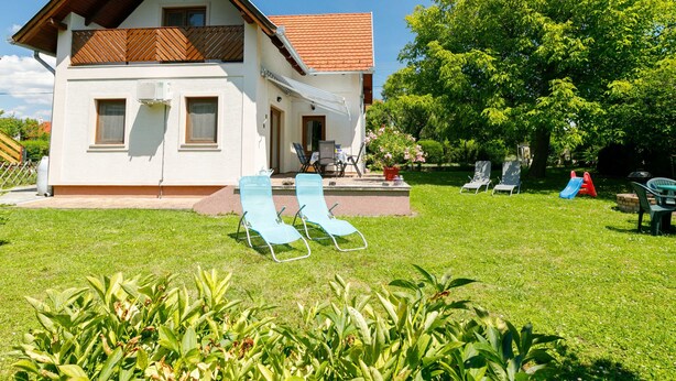 Een huis met twee verdiepingen, een schuin dak, een balkon en een patio met twee lounge stoelen.